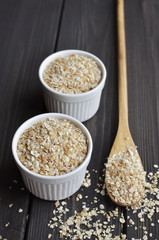 Rolled oats in bowls and spoon on dark wooden table background