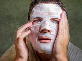 Fototapeta premium young funny and messy man applying beauty facial mask looking to the mirror surprised and horrified in skin care aging concept and male cosmetic face treatment