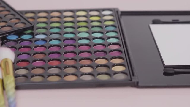 New eye shadow palette with makeup brushes on a pink background.
