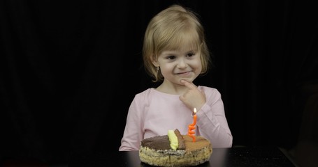 Little cute girl making a wish before blow out festive candle on birthday cake