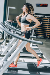 Attractive muscular smiling fitness woman running on treadmill in gym