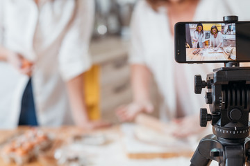 Culinary vlog. Two women baking shooting smartphone video tutorial. Content creating equipment. Online business hobby.
