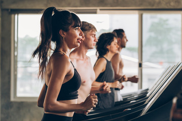 Young 20s Caucasian sporty group of men and women running together on treadmill in gym - Waist up shot - Fitness sports portrait