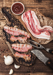 Grilled bacon strips on vintage wooden board with raw fresh smoked pork bacon on butchers paper...