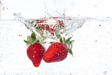 ripe red strawberries are thrown and dropped into sparkling water, many bubbles