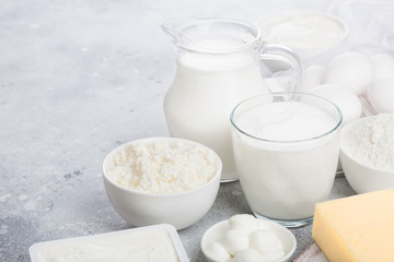 Fresh dairy products on white table background. Jar and glass of milk, bowl of sour cream, cottage cheese and baking flour and mozzarella. Eggs and cheese. Space for text