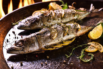 Grilled fish with various vegetables on pan on the flaming grill