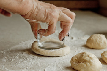 women's hands cut the raw kneaded dough into pieces on the background of the kitchen interior. cooking baking dish