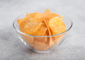 Glass bowl plate with potato crisps chips with paprika on light table background.