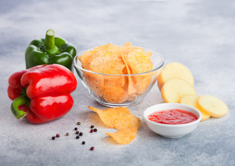 Glass bowl plate with potato crisps chips with paprika on light table background. Red and green paprika pepper with potatoes and sweet chilli sauce.