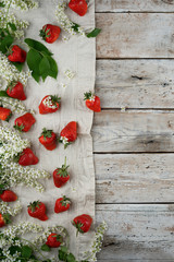 strawberry fruits and bird cherry blossom at the bottom on an old wooden textured table with copy space view from above. Summer frame