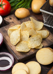 Fresh organic homemade potato crisps chips with sour cream and red onions on chopping board on dark wooden background. Tomatoes with green onion and bowl of ketchup.