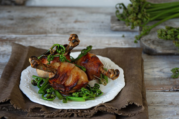 Chicken legs in bacon and fried bracken on a vintage plate. Fresh bracken on vintage chopping Board