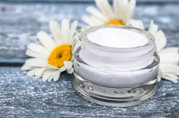 Obraz na płótnie Canvas Cosmetic cream in a glass jar stands near the daisies.