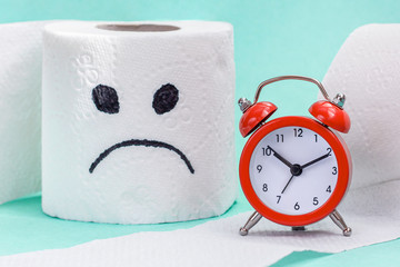 Constipation, indigestion, digestion problem. Alarm clock and toilet paper with sad face. Сreative concept