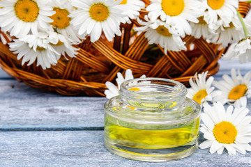 On the boards near the basket with chamomile flowers there is a bank of light chamomile essential oil.