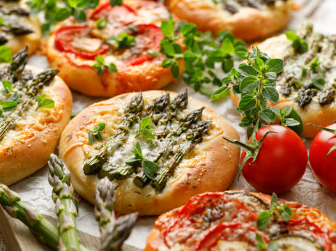 Mini pizzas with the addition of green asparagus, tomatoes, cheese and herbs, close-up. Vegetarian pizzas, delicious appetizer