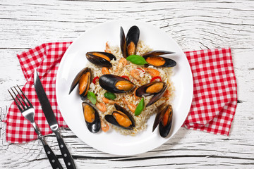 Fried rice with seafood mussels, shrimps and basil in a plate with towel, knife and fork on white cracked wooden table