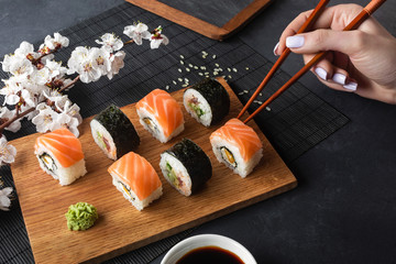 Set of sushi and maki rolls, hand with chopsticks and branch of white flowers on stone table