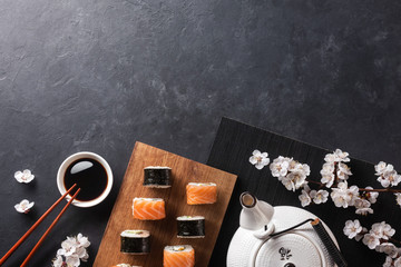 Set of sushi and maki rolls with branch of white flowers and teapot with the inscription green tea on stone table
