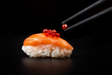 Red caviar in a chopsticks over sushi. Macro