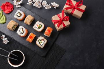 Obraz na płótnie Canvas Set of sushi, maki rolls, gift boxes with branch of white flowers on stone table