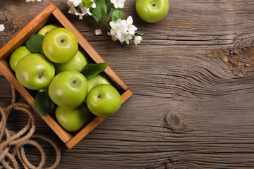 Ripe green apples with branch of white flowers in wooden box on a wooden table