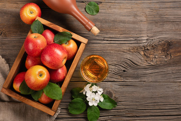 Ripe red apples in wooden box with branch of white flowers, glass and bottle of cider on a wooden...