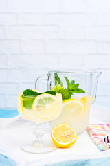 Lemonade with ice, lemon slices and mint in a glass and a carafe on a blue wooden table. Summer cold refreshing drink with fruits and vitamins.