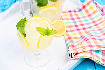 Lemonade with ice, lemon slices and mint in a glass and a carafe on a blue wooden table. Summer cold refreshing drink with fruits and vitamins.