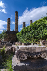Delphi, Phocis / Greece. Temple of Apollo and a Ionic order capital of an ancient column at the archaeological site of Delphi. Sunny day, cloudy sky