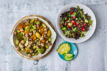 Baked, roasted, grilled vegetables in skillet with fresh summer salad and avocado pieces on white marble background with space for text. Vegan, vegetarian healthy food.