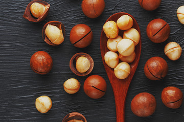 Shelled macadamia nut and peeled macadamia nut on a black textural background in a wooden spoon. Low contrast