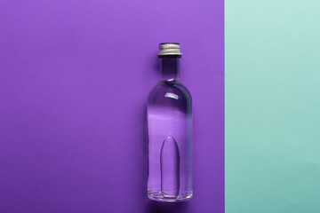 glass bottle with water on bright purple and azure background 