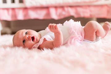 happy 1 month old baby girl laying on back on pink furry blanket from side