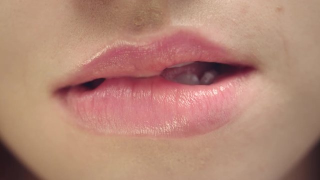 Female face of sensual woman biting and licking plump lips. Sexy lips and mouth