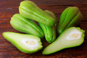 raw, fresh and organic chayote, whole and sliced on rustic wooden table