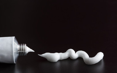tube of white cream, ointment stroke squeezed out on black background - obrazy, fototapety, plakaty