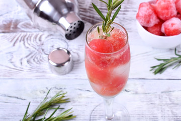 Sparkling cocktail with watermelon balls and rosemary in a champagne glass on white table