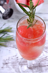 Sparkling cocktail with watermelon balls and rosemary in a champagne glass on white table