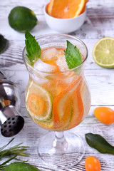 Sparkling beverage with slices of lime, kumquat and orange topped with mint against the white wooden background