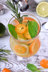 Sparkling beverage with slices of lime, kumquat and orange topped with mint against the white wooden background