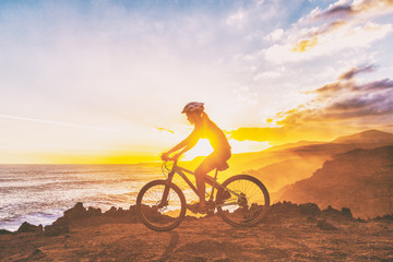 Mountain biking cyclist girl riding MTB bike on coast trail against sunset. Silhouetter of woman doing sports outdoors. Healthy and Active lifestyle.