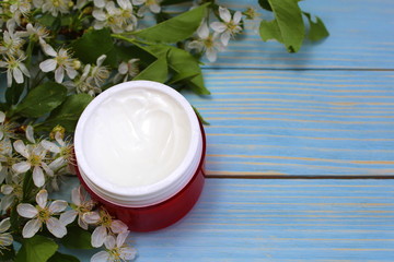 Cosmetic cream in a red container on the background of cherry flowers