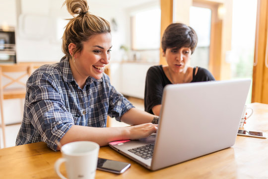 Two beautiful and young women having breakfast at home and using the laptop