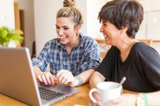 Two beautiful and young women having breakfast at home and using the laptop