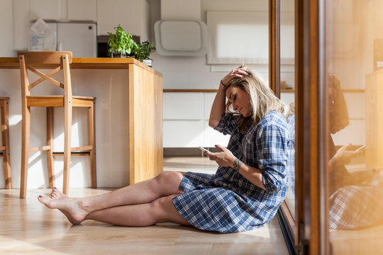 Beautiful and young woman sitting on the floor of her house on the mobile phone