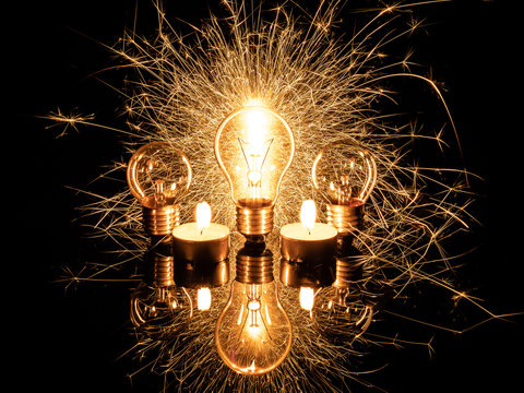 Light bulb with sparklers from behind and candles on black background