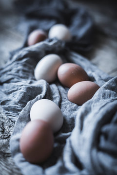 Bunch of chicken eggs lying in tablecloth on rustic wooden table.