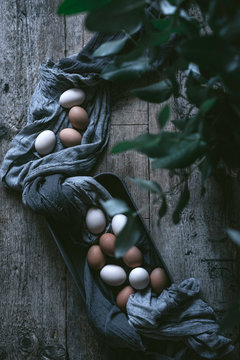 Bunch of chicken eggs lying in tablecloth inside oven tray on rustic wooden table with plant twigs